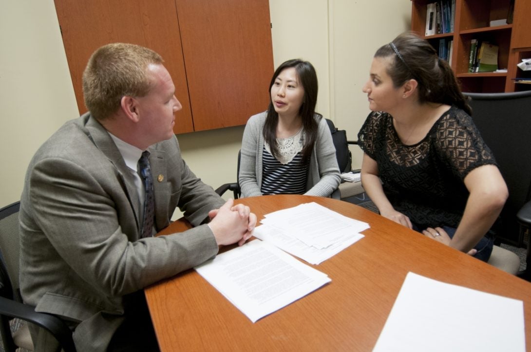 Students speaking to professor at a desk