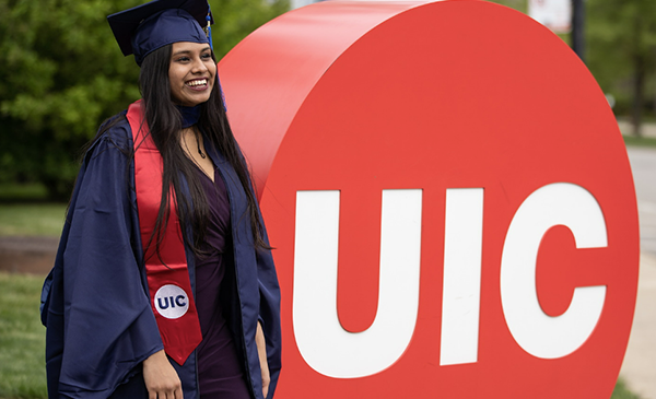Graduate standing in front of UIC sign in regalia